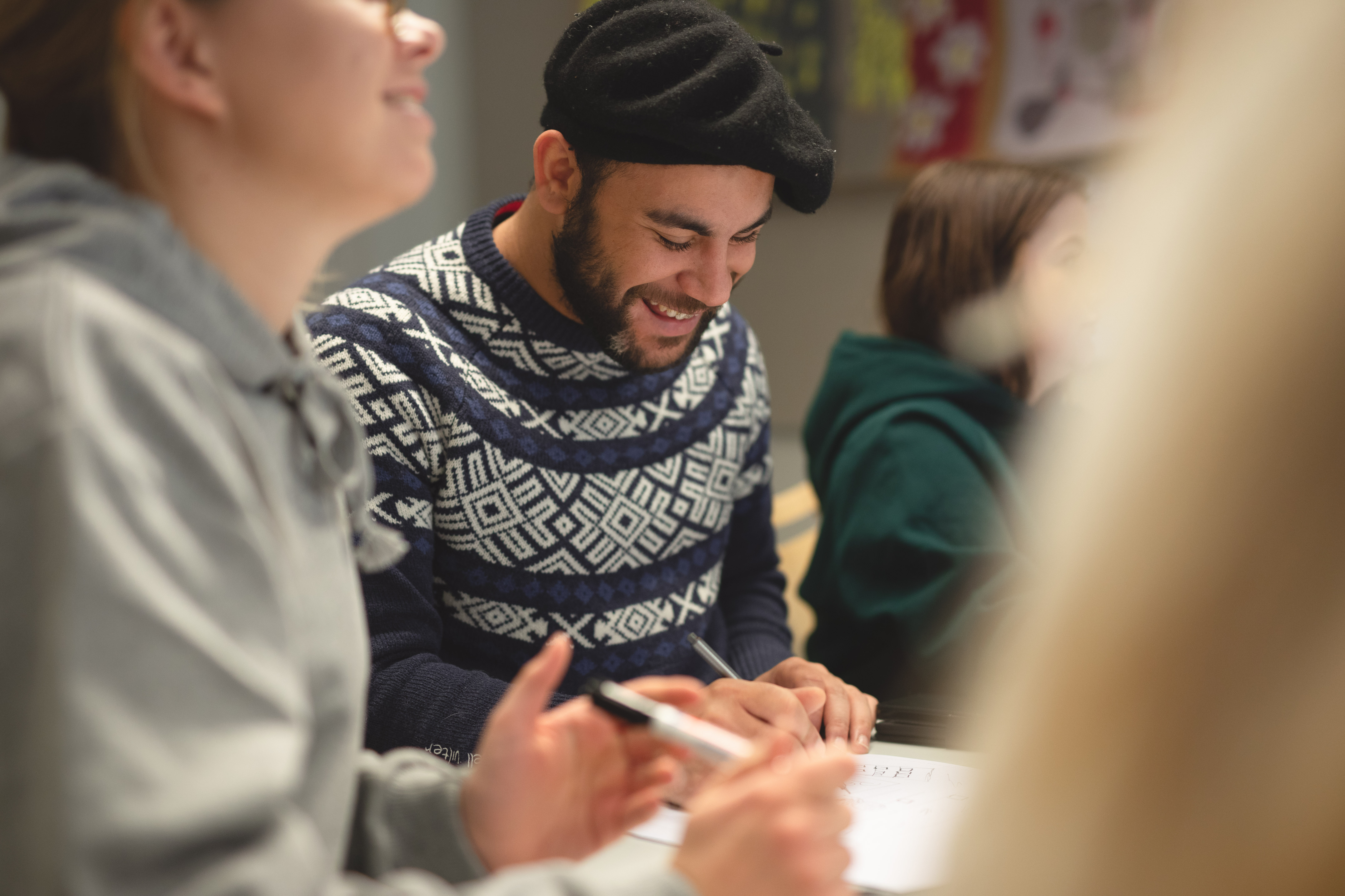 En student sitter mellom to andre studenter, han ser ned og smiler. 