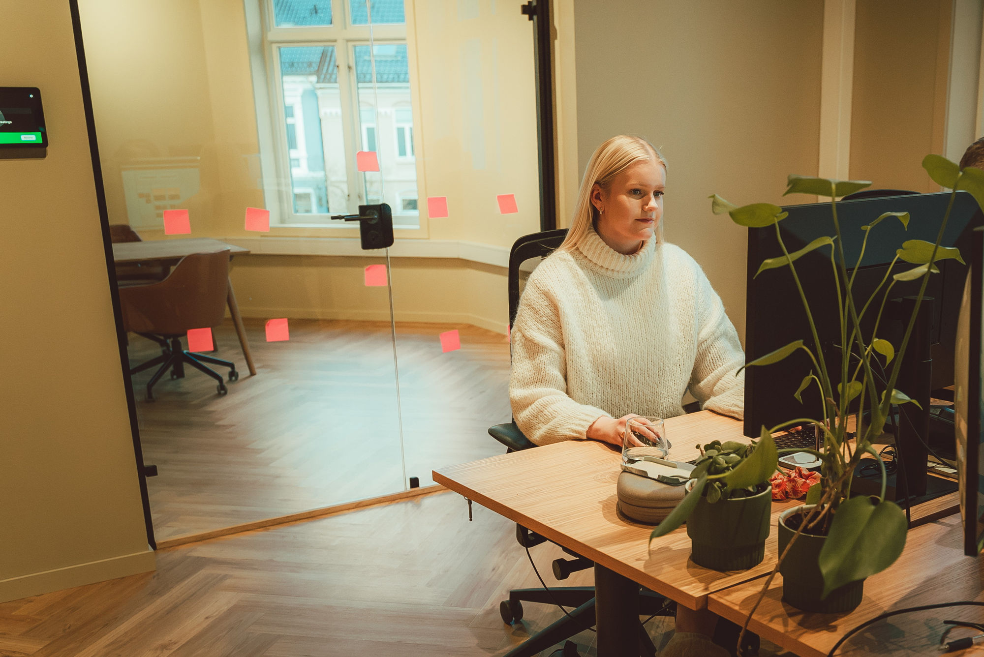 Lene jobber ved en PC på kontoret. På speilet bak henne henger post-it-lapper som beskriver ulike prosesser.