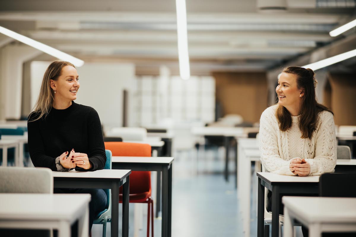 To studenter på høyskolen kristiania som sitter i et tomt klasserom