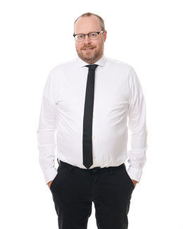 Mann med briller. hvit skjorte, svart slips, svarte bukser.
