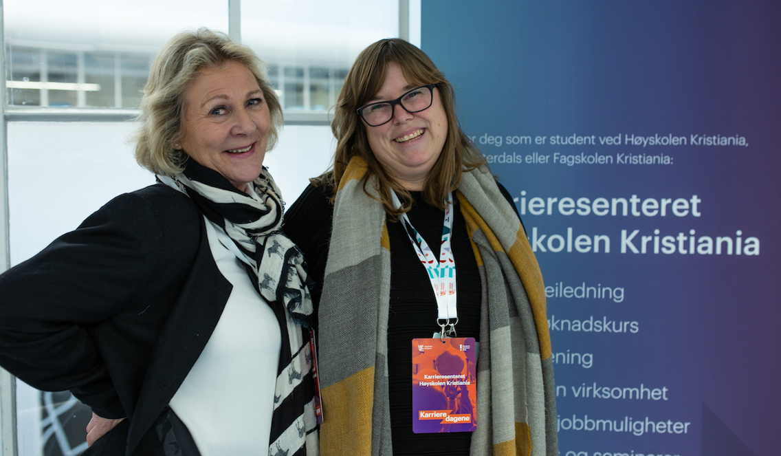 Laila Olsen og Mette Lise Martinsen fra karrieresenteret står standhaftig ved en plakat for hvor reklamerer for karrieresenteret til Høyskolen Kristiania.