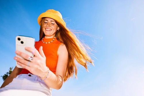 En ung kvinne ser ned på telefonen sin og smiler