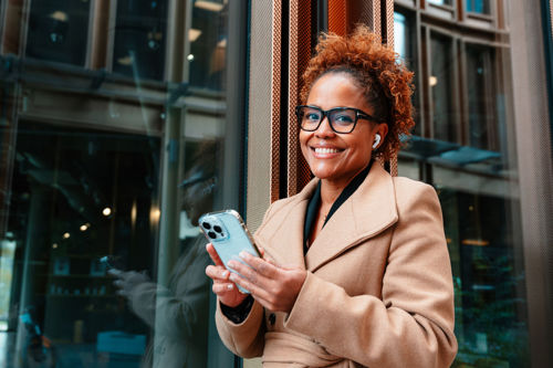 Nettstudent med mobiltelefon poserer foran glassfasade.