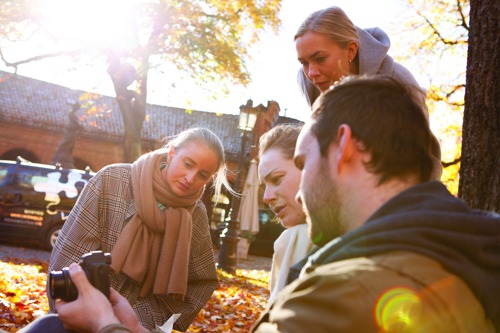 Fire studenter på digital innholdsproduksjon er samlet rundt et kamera, som de alle ser på.