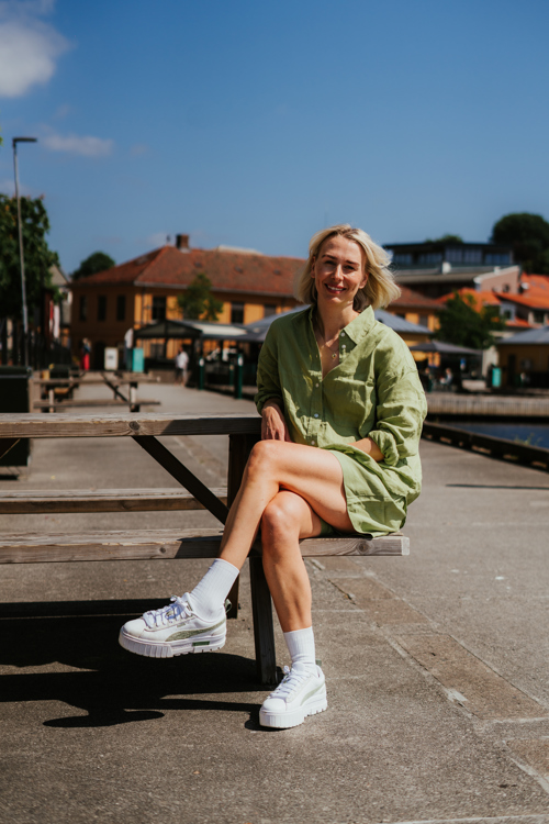 Smilende ung kvinne sitter på en parkbenk med Halden marina i bakgrunnen.