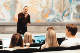 Foto av studenter i en forelesning vendt mot lærer som gestikulerer