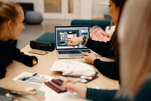 Bilde av studenter som peker på laptop med skissebøker rundt.
