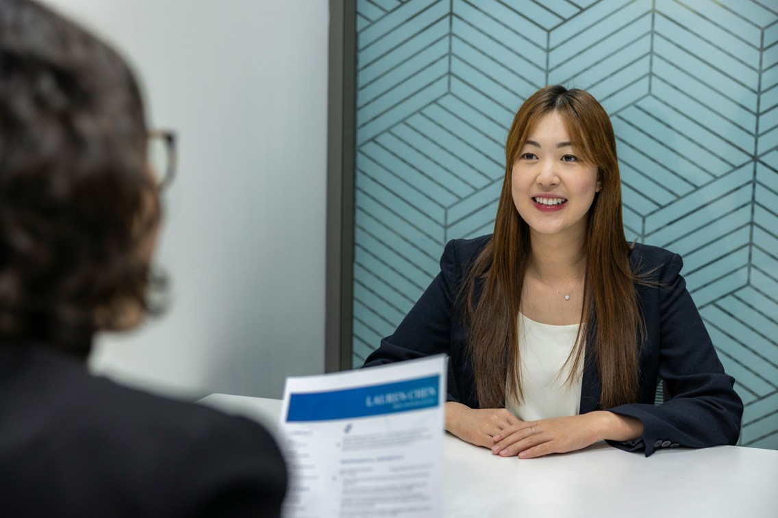 Kvinne som sitter og smiler mot en dame som holder CV-en hennes i hånda