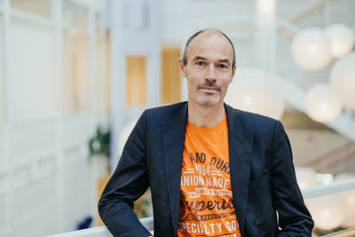 Mann i oransje t-skjorte med mørkblå dressjakke over.