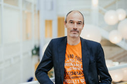 Mann i oransje t-skjorte med mørkblå dressjakke over.