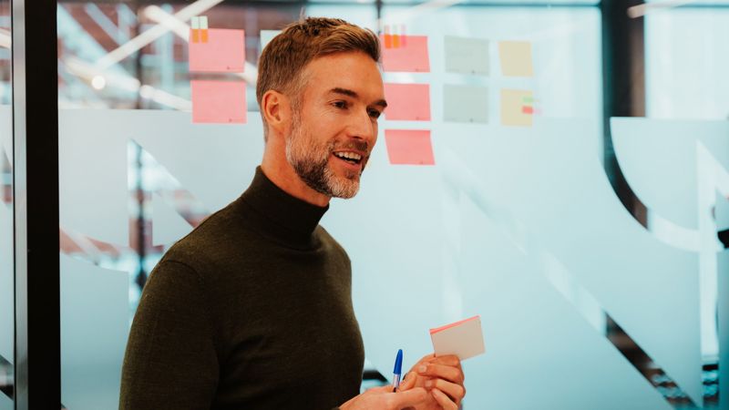 Mann står foran ulike postit-lapper som er festet til en glassvegg. 