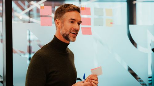 Mann står foran ulike postit-lapper som er festet til en glassvegg.