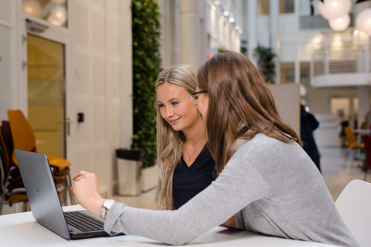 Foto av to kvinner foran en laptop i høyskolelobby.