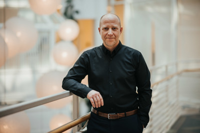 Foto av mann i sort skjorte som støtter seg på et rekkverk.