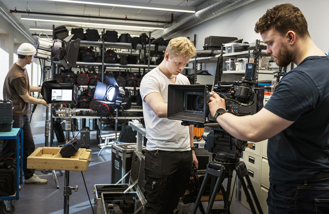 Tre studenter rigger store filmkameraer i utstyrslager.