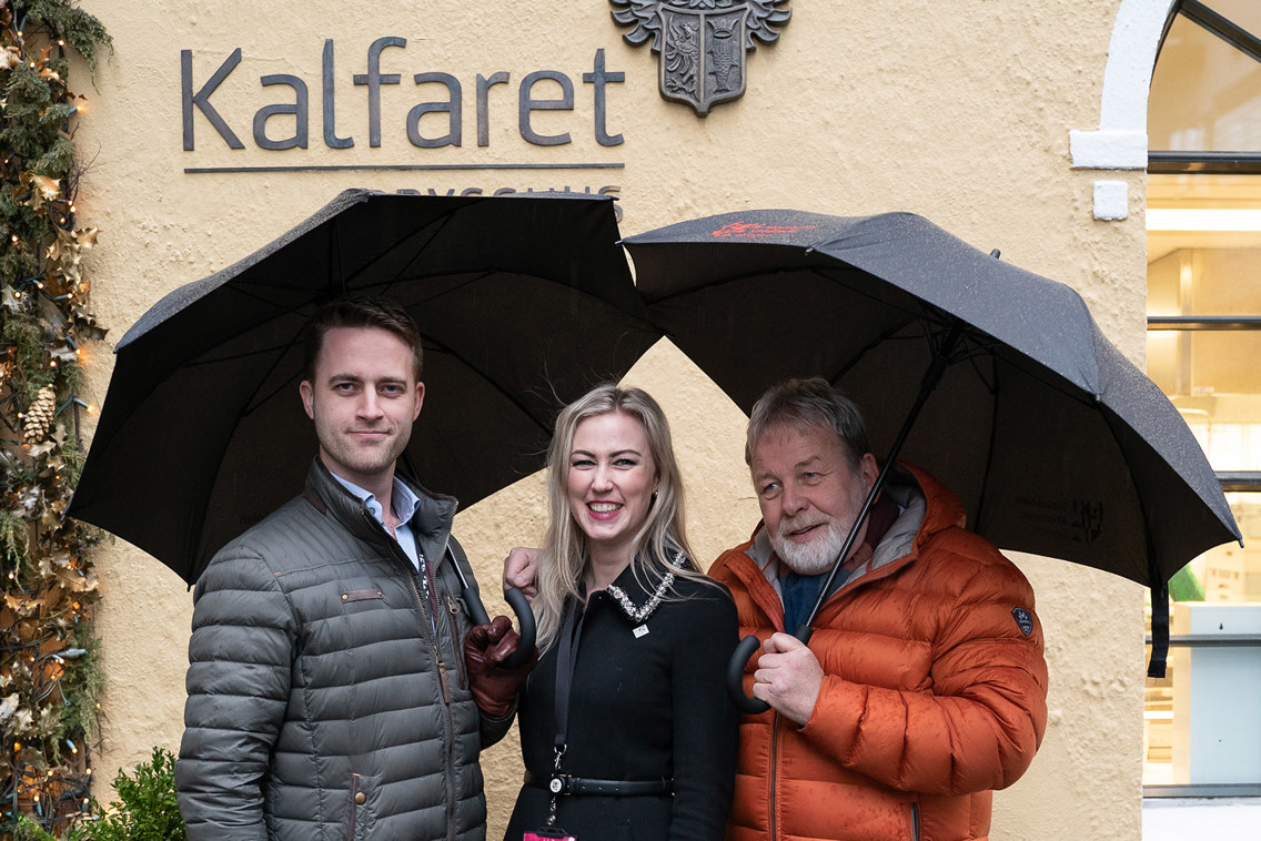 Foto at to menn og en kvinne, med paraplyer.