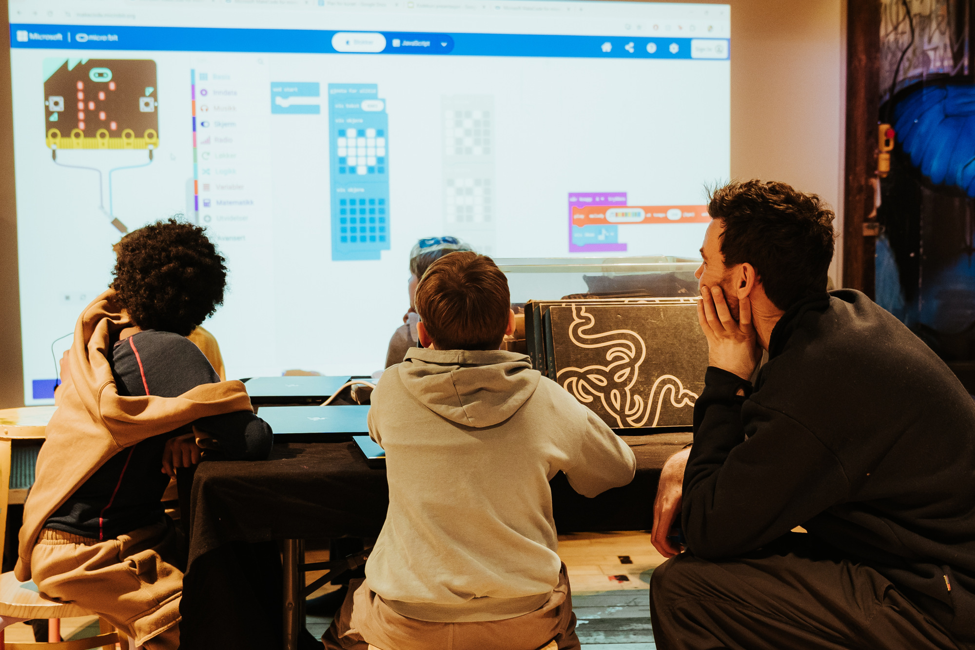 En mann som viser barna koding, fremfor en skjerm som viser koding av spill. 