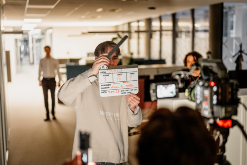 Student gjennomfører et filmopptak med klapper foran et kamera i et innendørs opptaksmiljø.