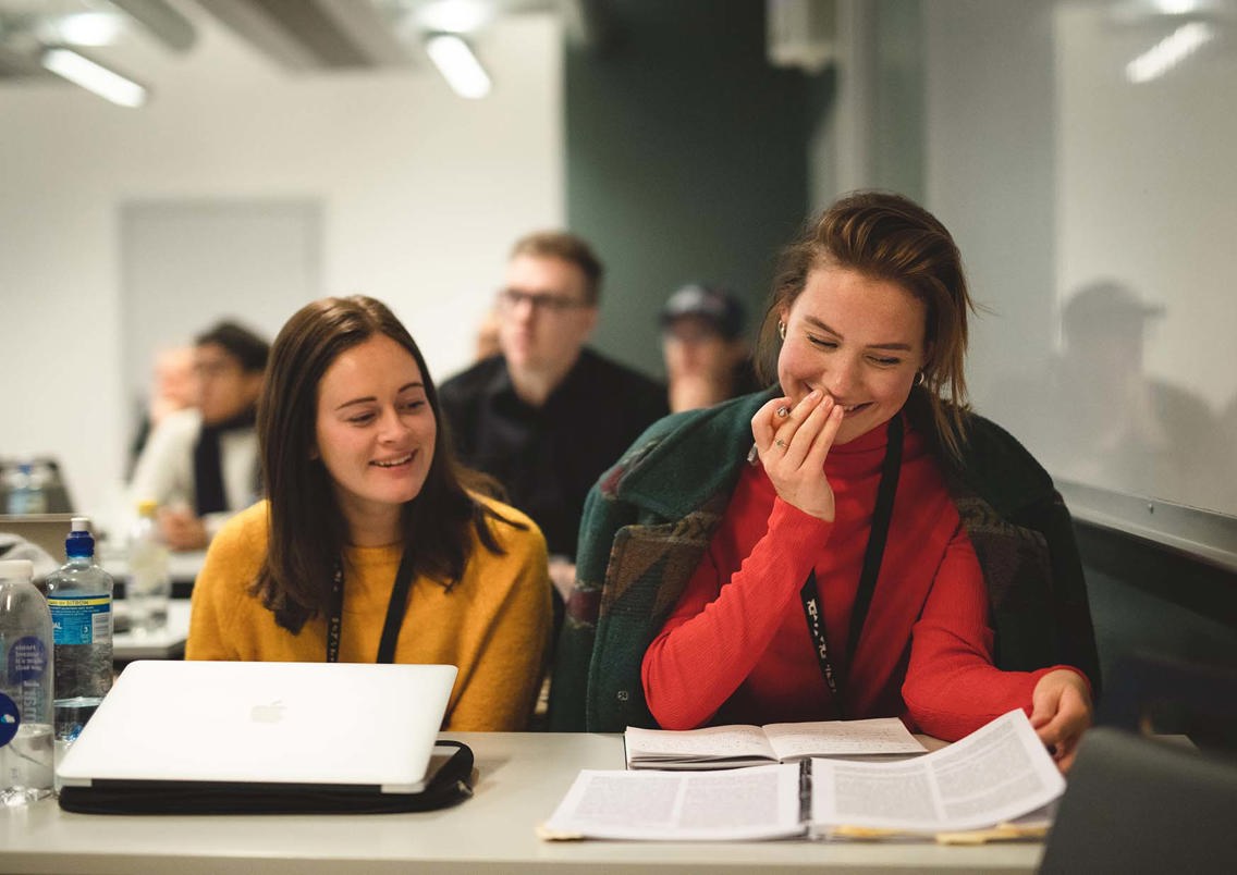 Foto av to studenter som leser i samme bok.