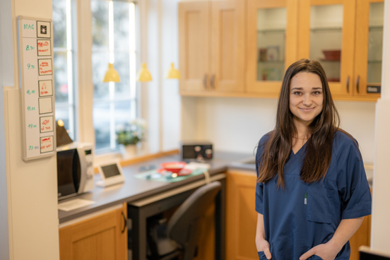 Helsefagarbeider i arbeidsantrekk står i et kjøkkenmiljø med ulike typer velferdsteknologisk utstyr på benken