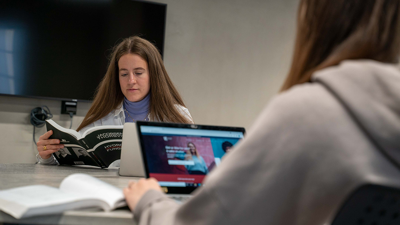 Foto av to kvinnelige studenter som leser og jobber med PC.