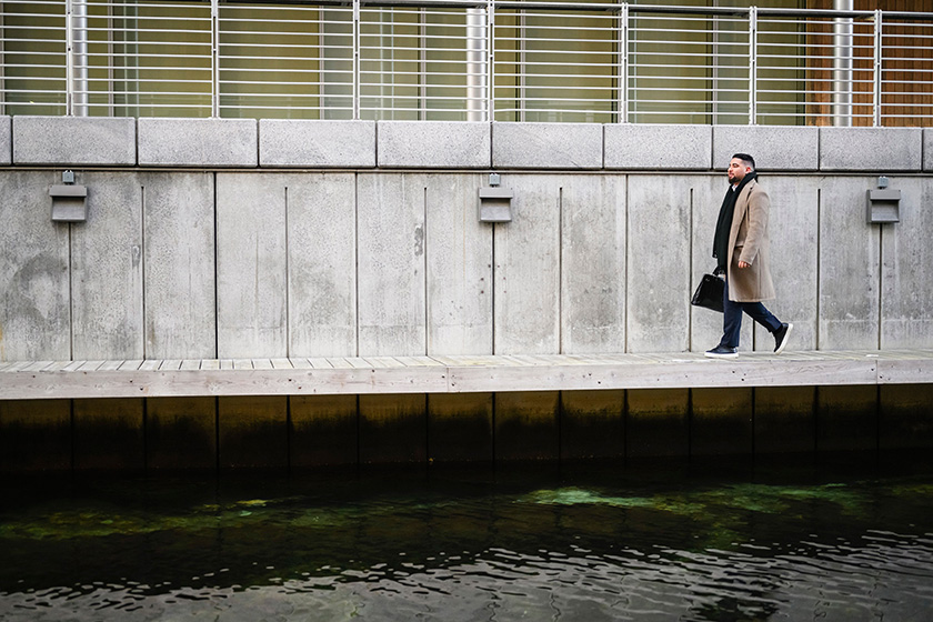 Mann med frakk og koffert går langs brygge.