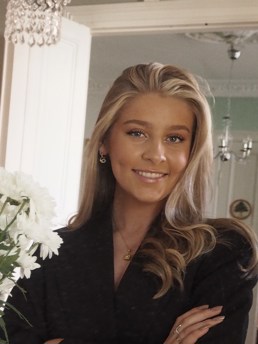 Portrett av interiørstudenten Stina Eline Brandåstrø som vant konkurransen på Fagskolen Kristiania. Hun har blondt hår, en svart skjorte på seg og smiler til kameraet.