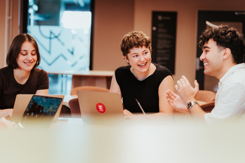 Tre studenter samarbeider med PC-er i et kontorlandskap.