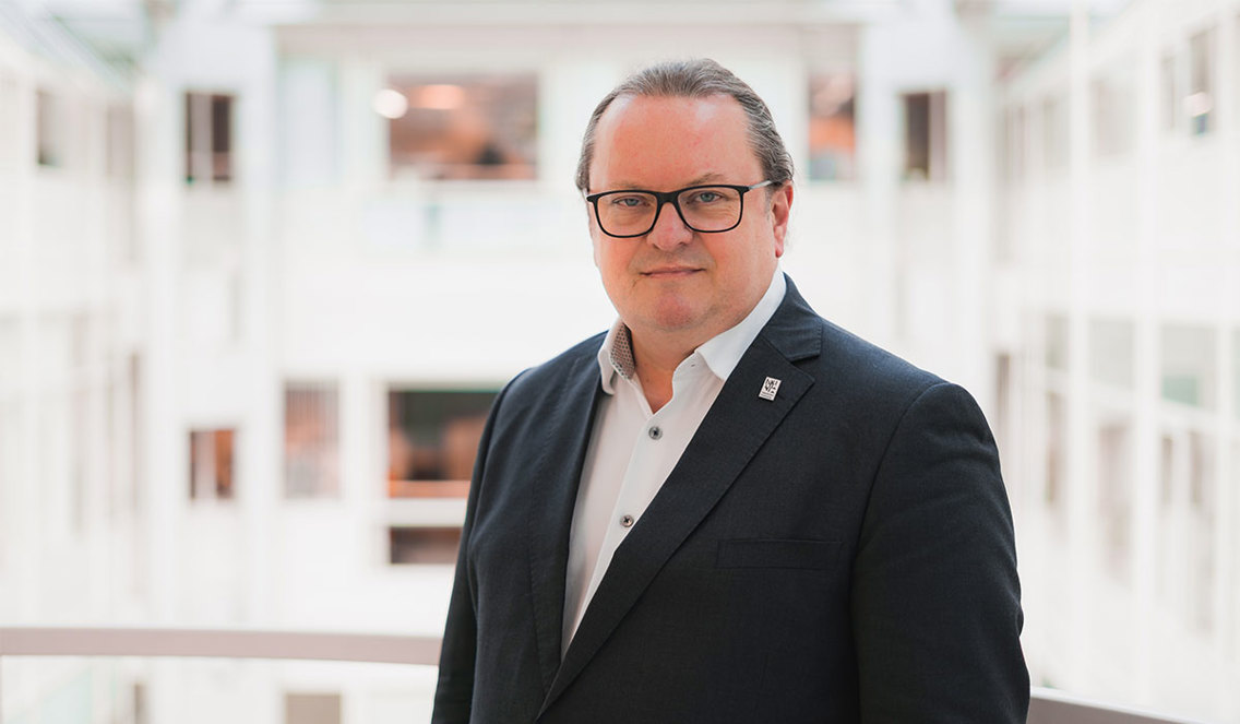 Mann i dress foran et lyst, åpent rom.