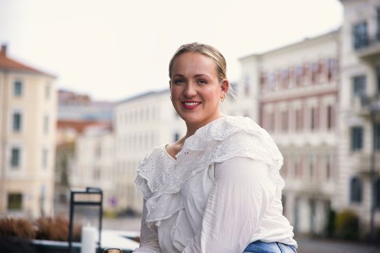 Frida sitter på en takterasse, med gamle murbygninger bak seg.