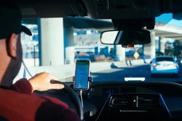 Mann som kjører bil og bruker GPS på telefonen.