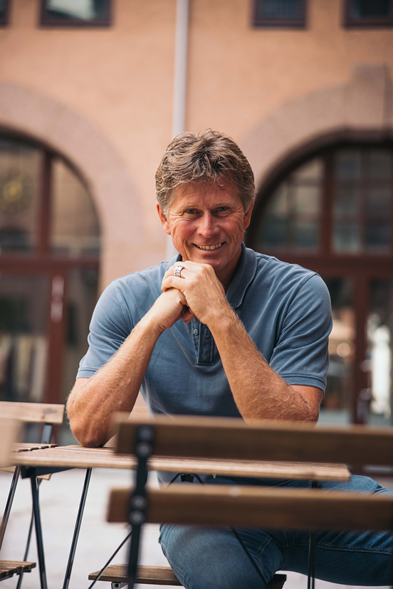 Foto av Rune Bjerke, sittende med foldede hender på en benk.