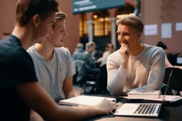 Foto av unge mannlige studenter som sitter rundt et bord med laptop, pensumbøker og notatblokker.