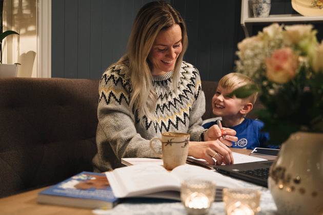 Miniatyrbilde fra videosnutt. En voksen og et barn smiler og ser på en bok sammen ved et bord, omgitt av en koselig atmosfære med stearinlys og blomster.