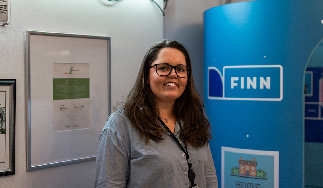Foto av kvinne som smiler foran Finn-logo på et kontor.