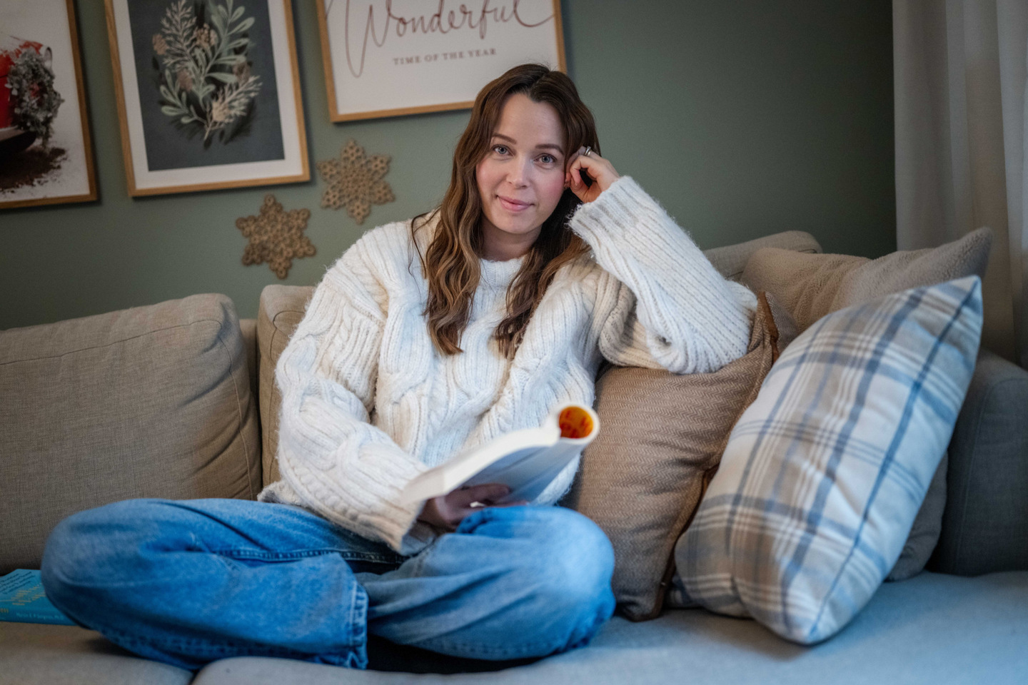 Monica som sitter på en sofa med bok i hånden og kryssede ben