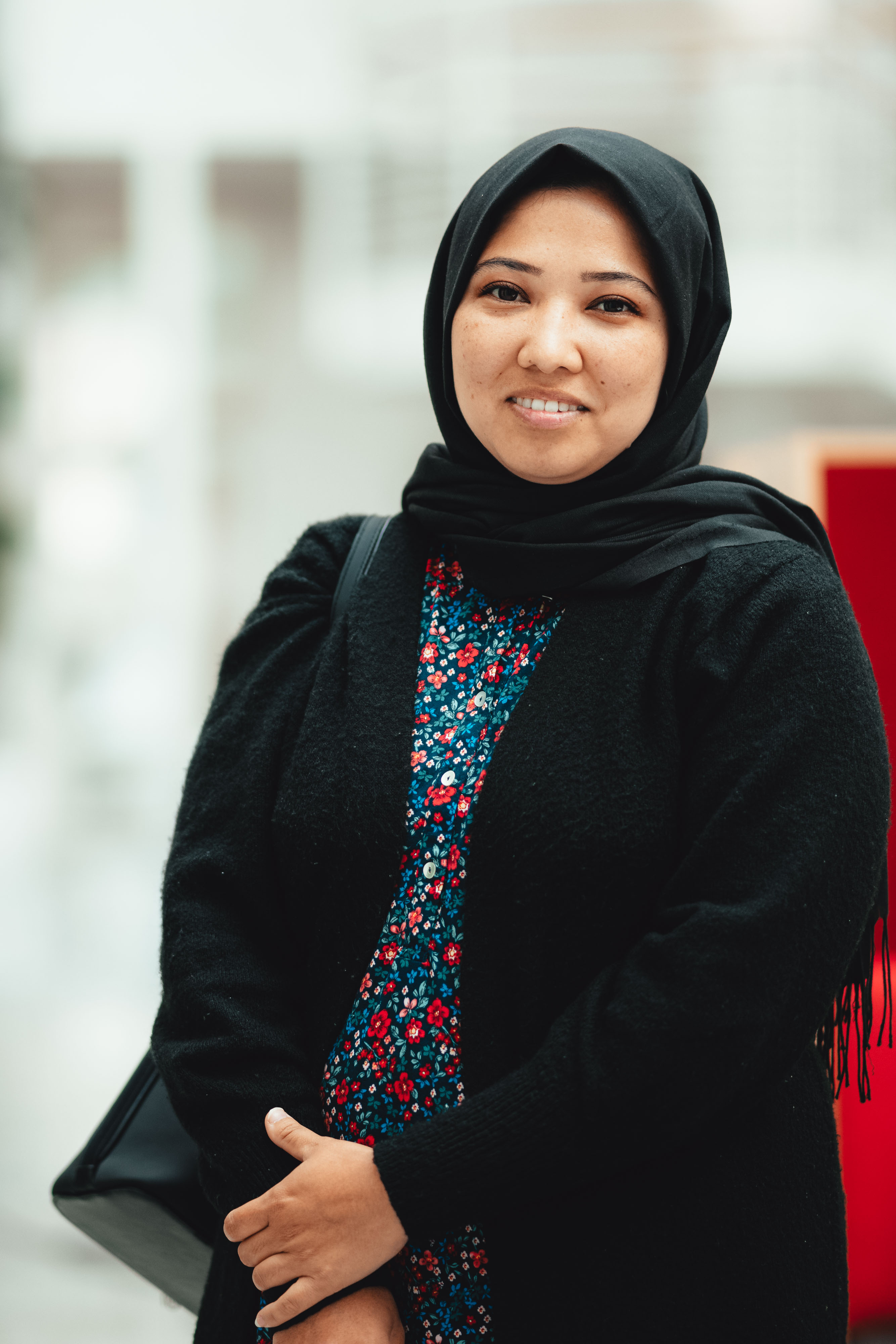 Ung kvinne i hijab og blomstrete skjorte smiler til kameraet.