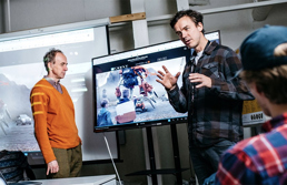 Foto av to mannlige forelesere foran en TV-skjerm.