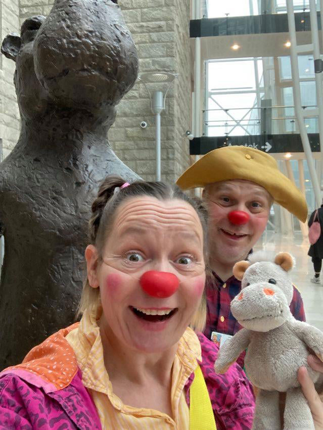 Klovne par tar selfie foran statue av flodhest på et sykehus.