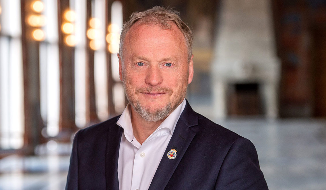 Blid mann i en stor hall står og ser i kamera.