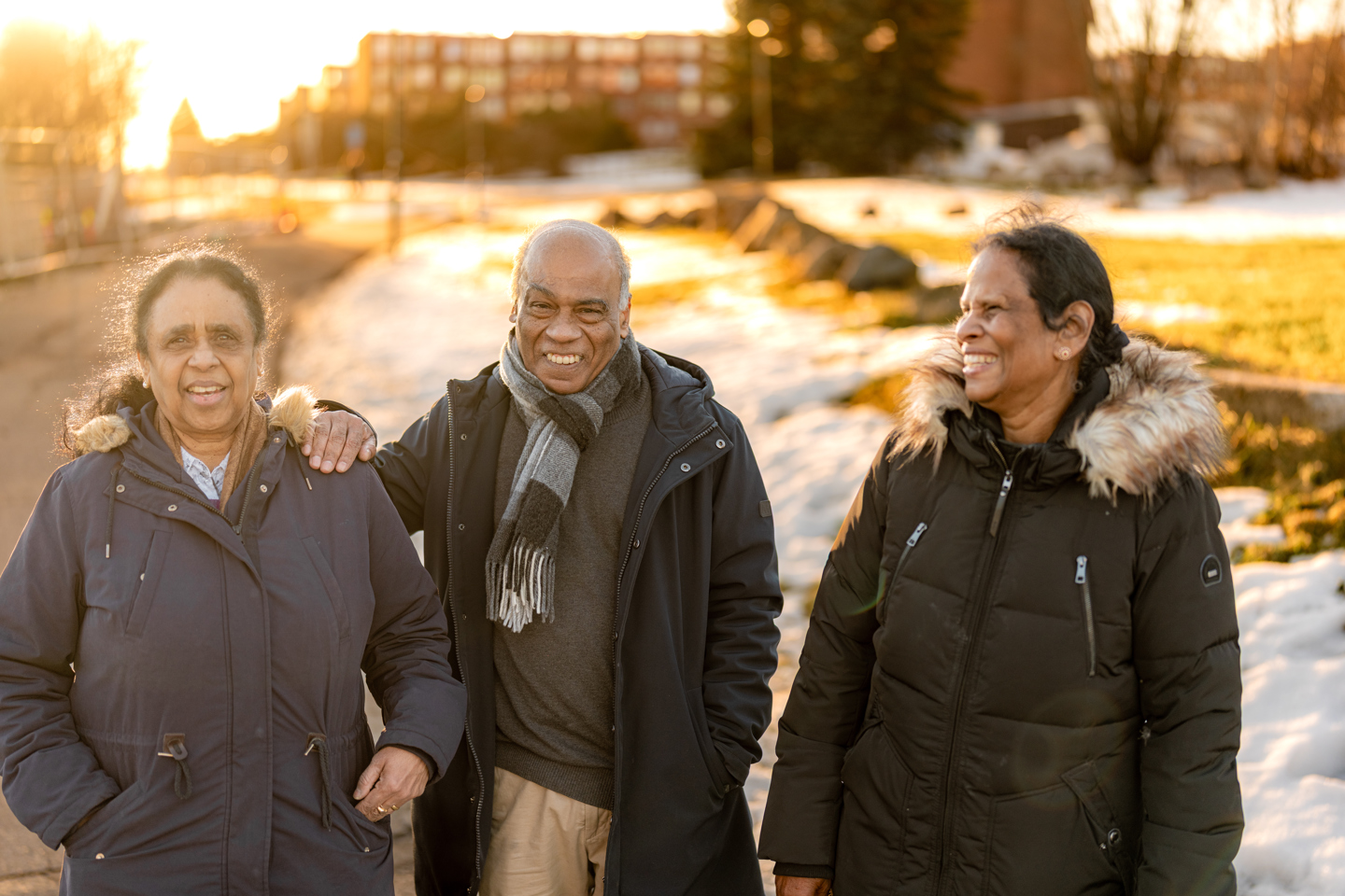 Tre voksne går sammen utendørs og smiler