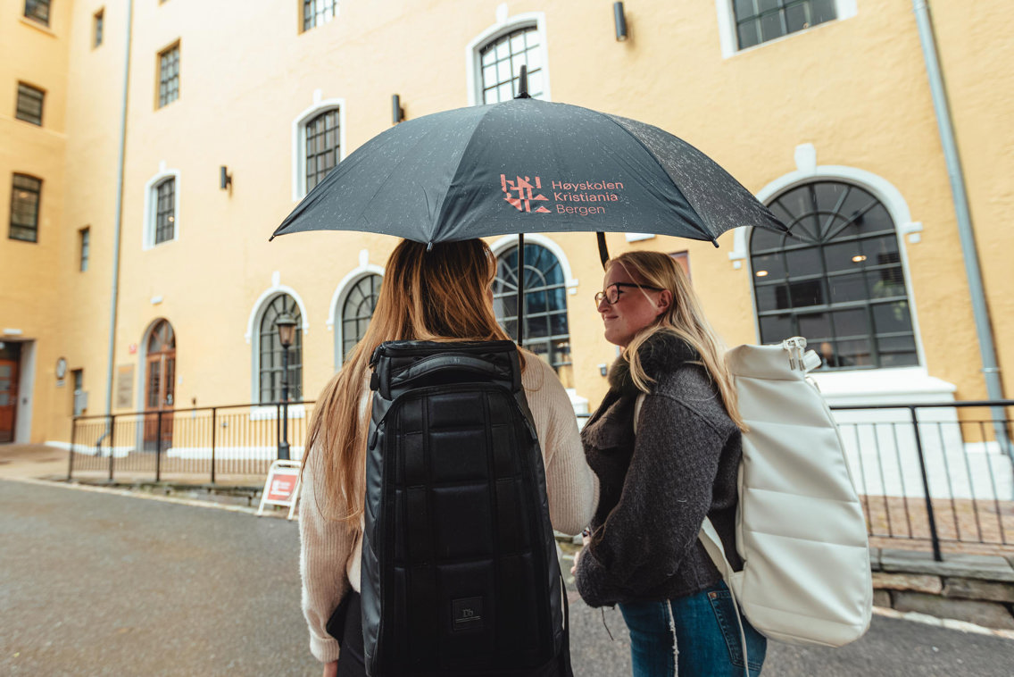 Tre studenter under en paraply med Kristiania-logo.