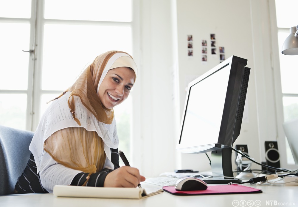 Kvinne i hijab jobber foran datamaskin.