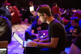 En mann sitter på pc-en i et rom med masse mennesker som også er på sin egen skjerm
