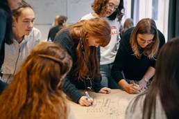 Foto av studenter samlet rundt et bord som drodler på et stort ark.