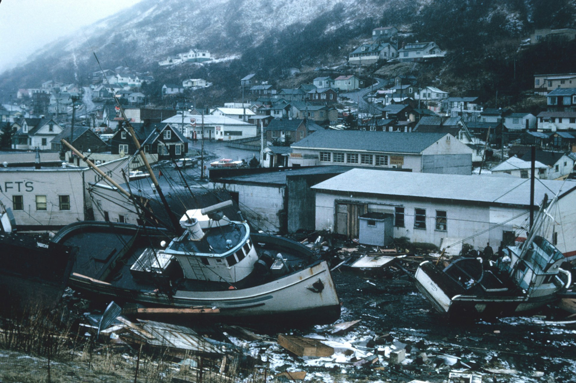 Båt som har havnet på land mellom hus i et landskap med snø og tåke og fjell