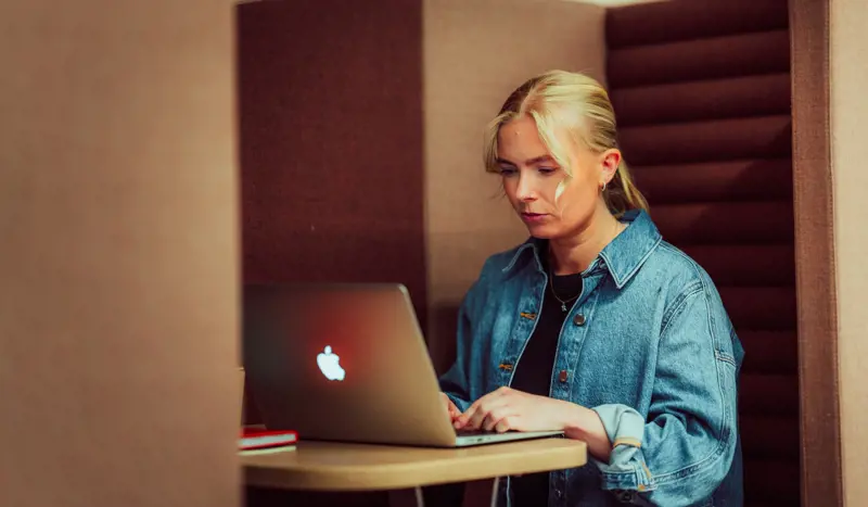 Jente sitter og jobber på en Mac