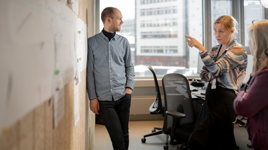 Tre personer samarbeider i en workshop ved en tavle i et møterom.