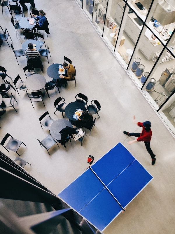 Bilde fra en høyskole eller et universitet, hvor noen studenter spiser lunsj og andre spiller bordtennis.