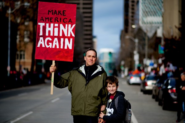En far og en sønn holder en plakat hvor det står "Make Ameria Think Again"